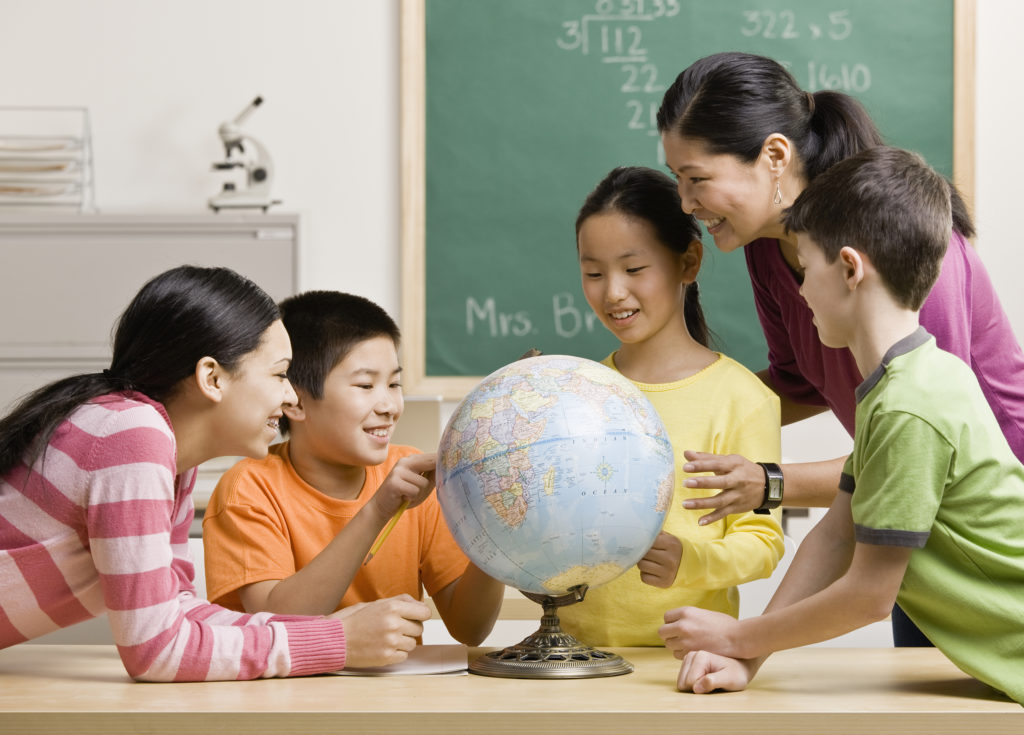 children looking at a globe on a teachers desk